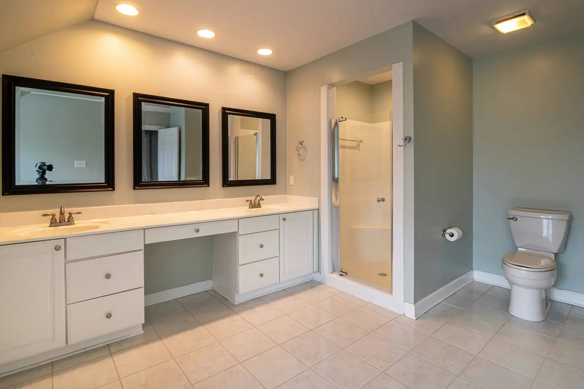 Primary bathroom with double mirrors, long vanity, tile floor, toilet, and glass shower