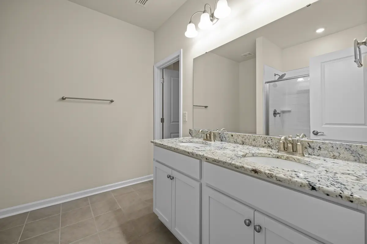 Finished bathroom vanity with stone counter, mirror, shower, towel bar, and tile floor