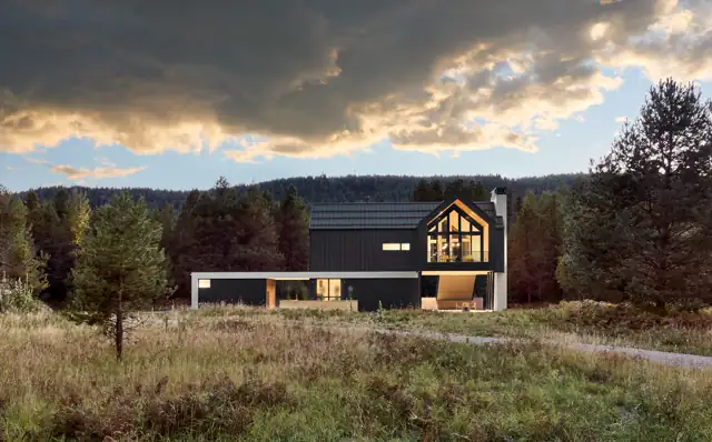 Modern Wisconsin home with a steep dark roof, wooded setting, and warm evening light