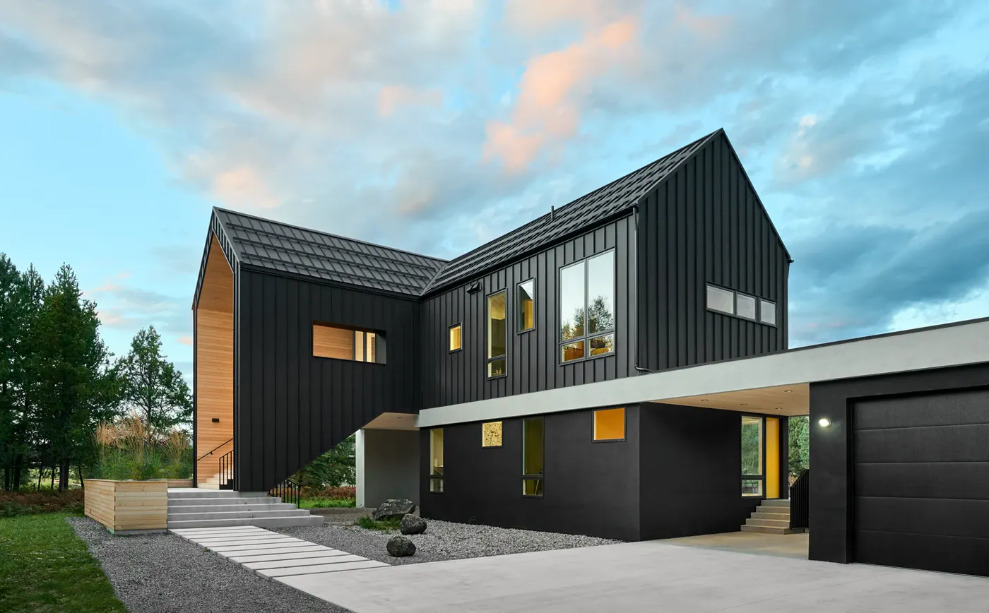 Complex standing-seam metal roof with valleys, garage access, and driveway staging on a wooded home