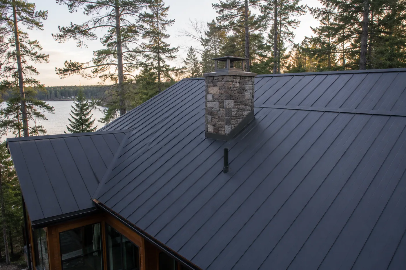 Standing-seam metal roof on a Wisconsin lake home with chimney and wooded surroundings